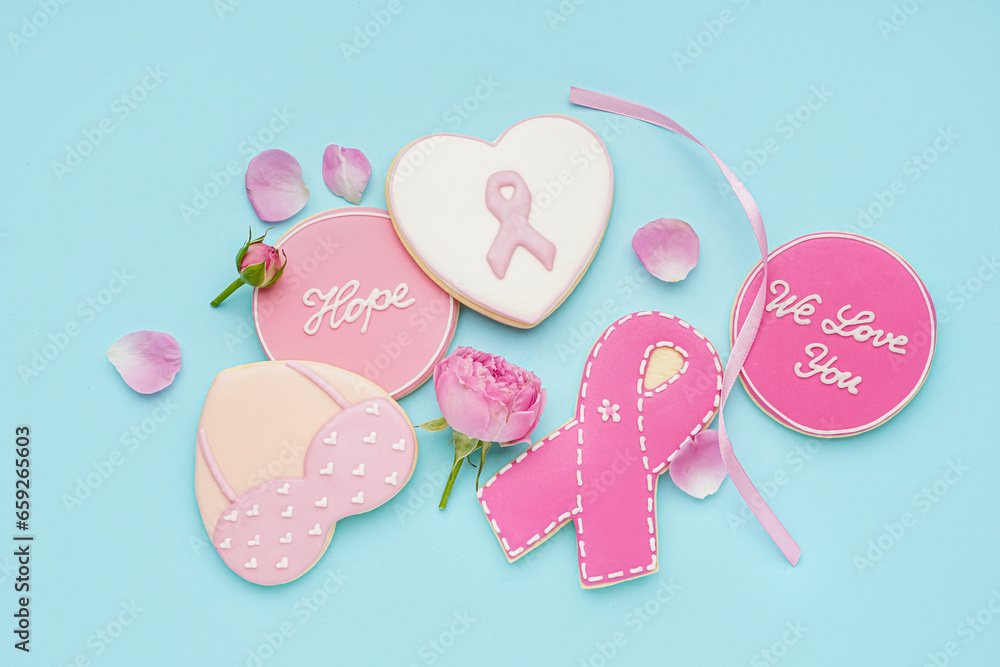 Pink cookies with ribbons, flowers and supportive words on blue background. Breast cancer awareness concept