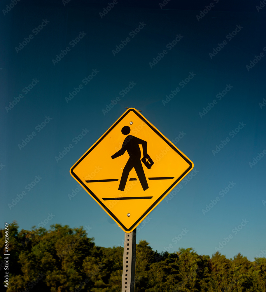 Traffic sign with graphic of a person crossing a street with a bible against a blue sly background Traffic sign with graphic of a person crossing a street with a bible against a blue sly background