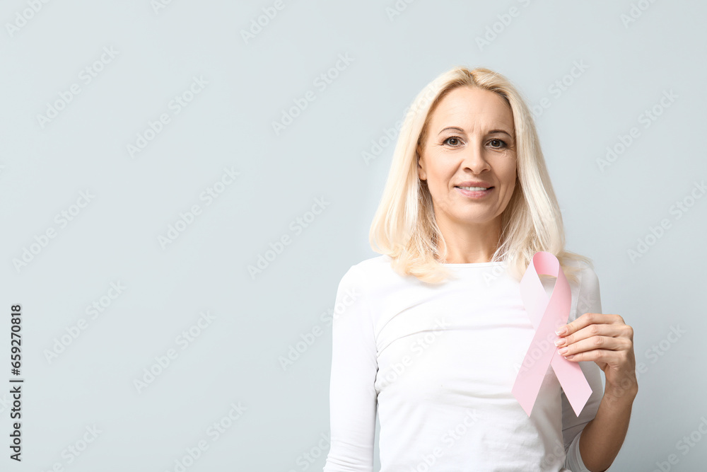 Mature woman with pink ribbon on grey background. Breast cancer awareness concept Mature woman with pink ribbon on grey background. Breast cancer awareness concept