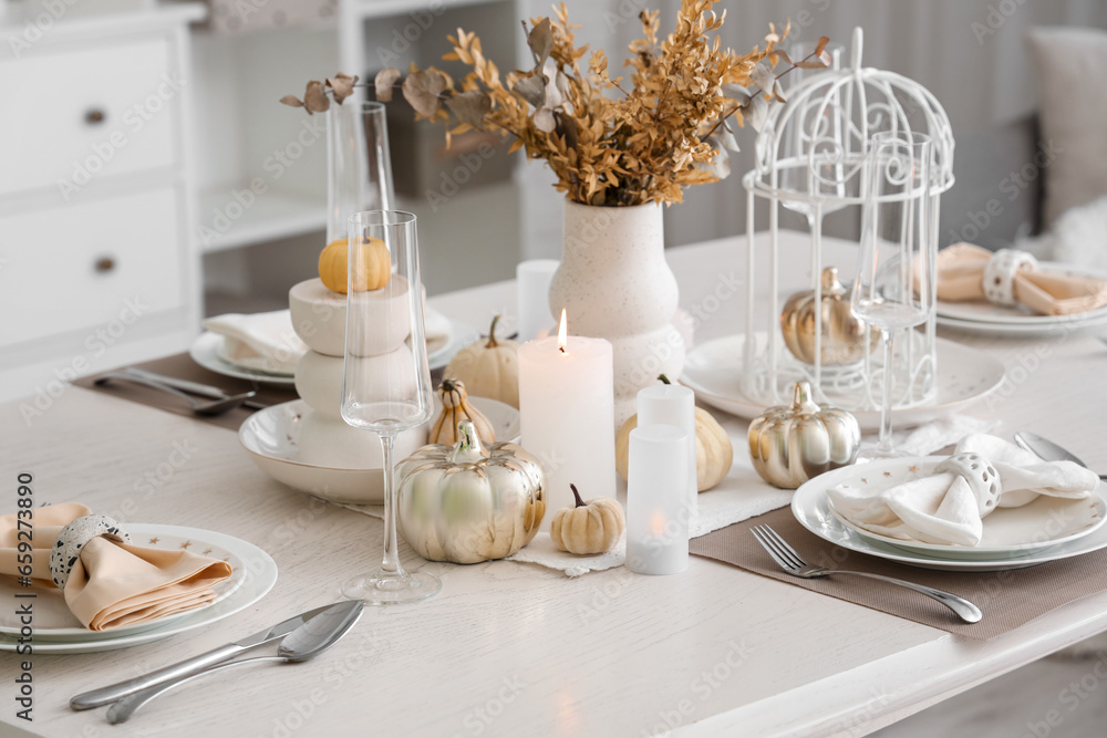Elegant table serving with pumpkins and burning candles for Thanksgiving dinner in light room Elegant table serving with pumpkins and burning candles for Thanksgiving dinner in light room
