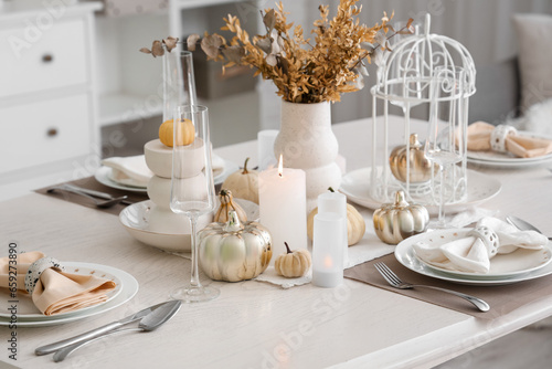 Elegant table serving with pumpkins and burning candles for Thanksgiving dinner in light room
