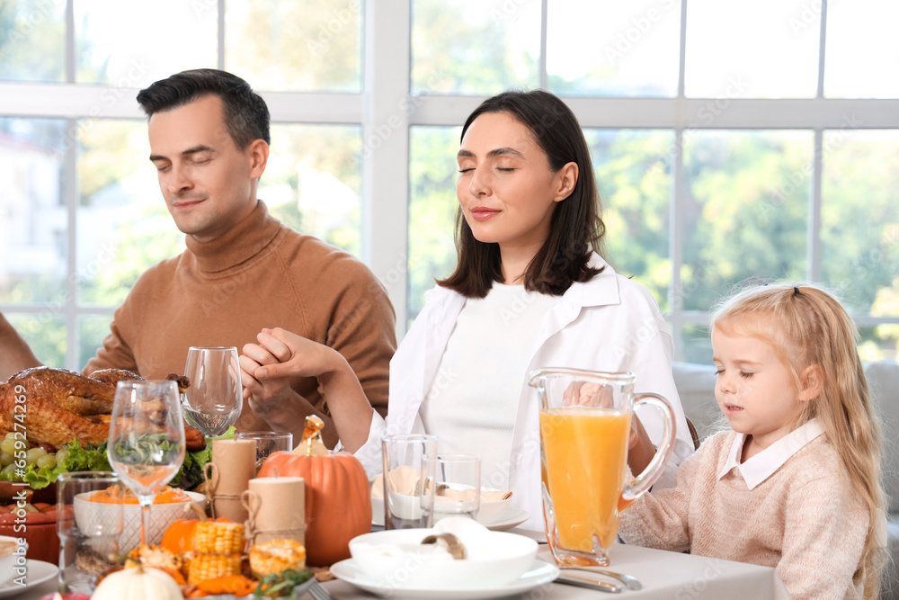 Happy family praying before dinner at festive table on Thanksgiving Day Happy family praying before dinner at festive table on Thanksgiving Day