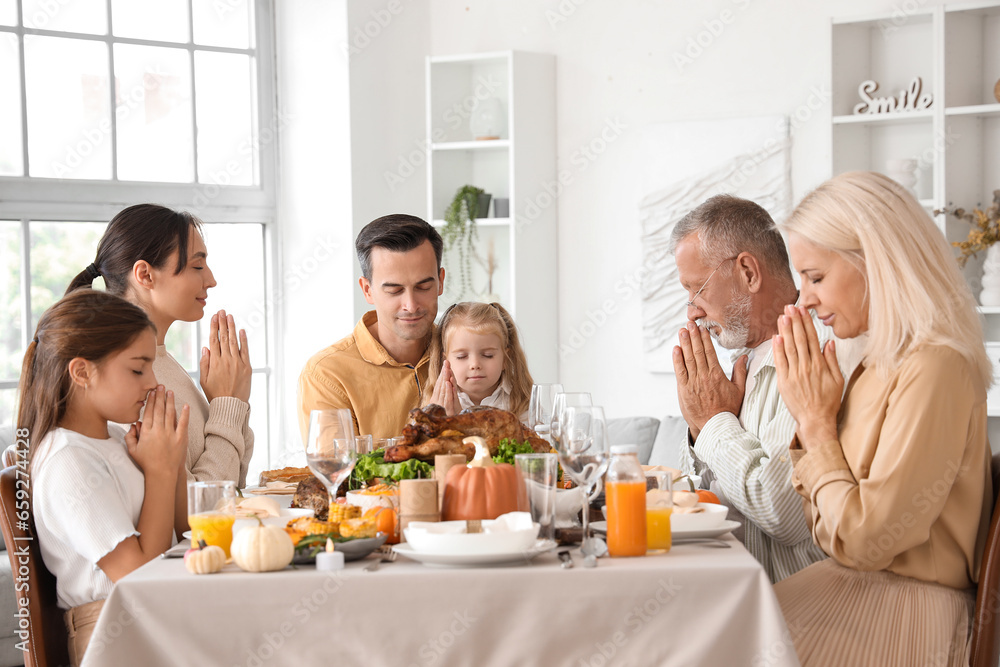 Happy family praying before dinner at festive table on Thanksgiving Day Happy family praying before dinner at festive table on Thanksgiving Day