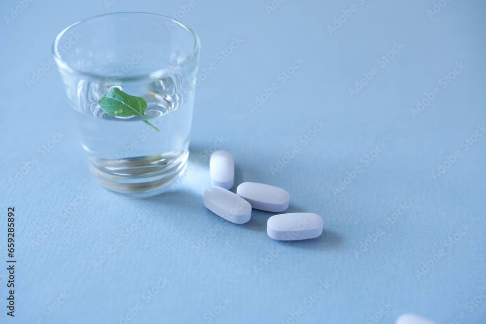 Pills and a glass of water on a blue background with copy space