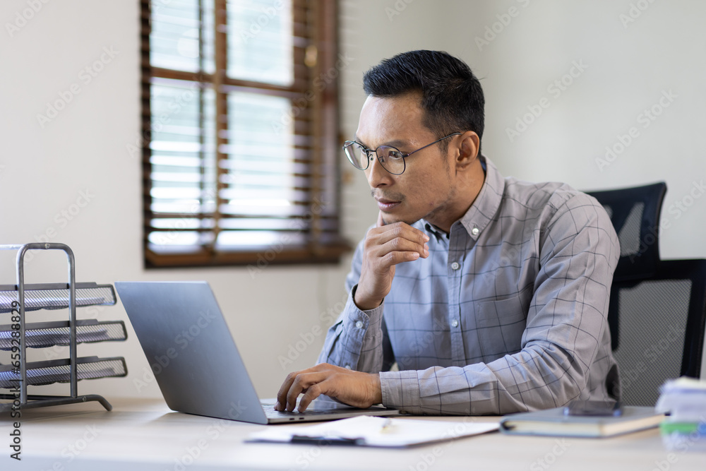 Fototapeta premium Portrait of Stylish Asian Businessman Works on Laptop, Does Data Analysis and Creative Designer, Looks at Camera and Smiles. Digital Entrepreneur Works on e-Commerce Startup Project