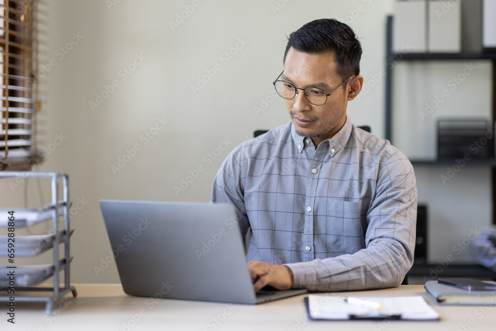 Portrait of Stylish Asian Businessman Works on Laptop, Does Data Analysis and Creative Designer, Looks at Camera and Smiles. Digital Entrepreneur Works on e-Commerce Startup Project Portrait of Stylish Asian Businessman Works on Laptop, Does Data Analysis and Creative Designer, Looks at Camera and Smiles. Digital Entrepreneur Works on e-Commerce Startup Project