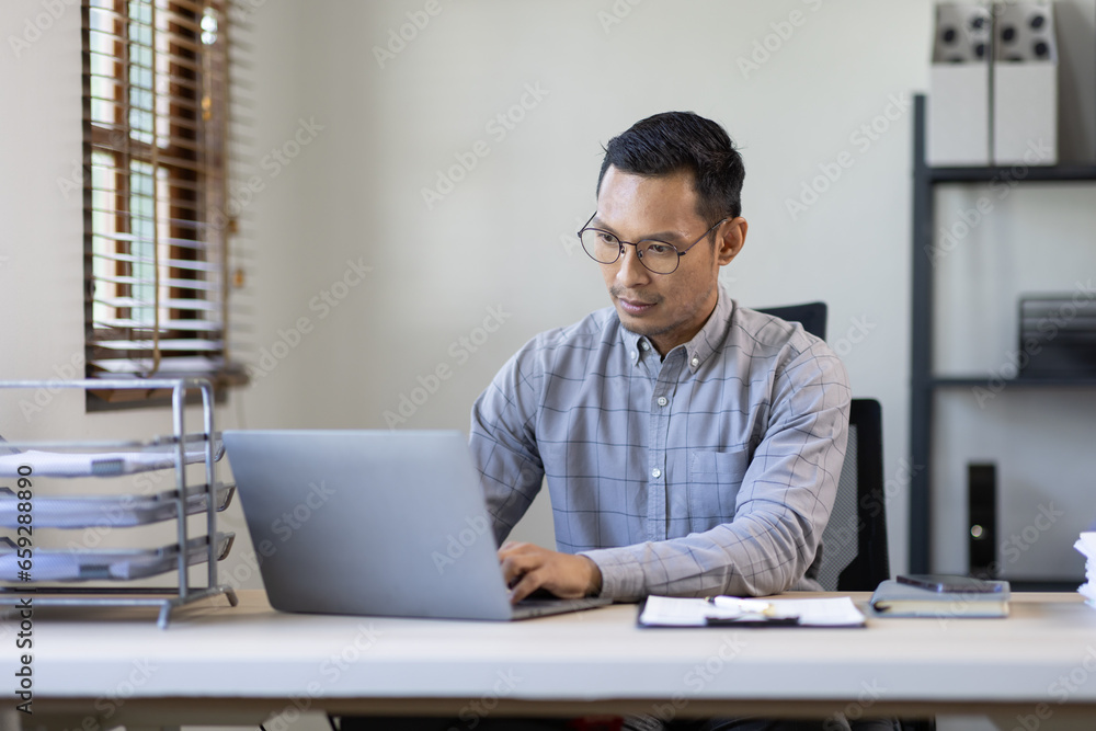 Portrait of Stylish Asian Businessman Works on Laptop, Does Data Analysis and Creative Designer, Looks at Camera and Smiles. Digital Entrepreneur Works on e-Commerce Startup Project Portrait of Stylish Asian Businessman Works on Laptop, Does Data Analysis and Creative Designer, Looks at Camera and Smiles. Digital Entrepreneur Works on e-Commerce Startup Project
