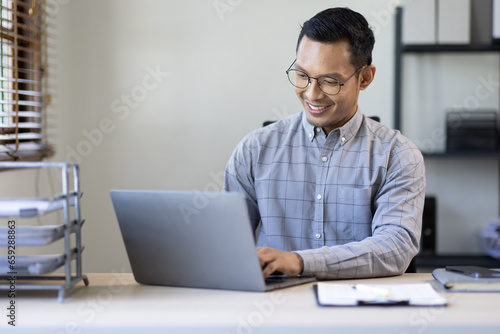 Portrait of Stylish Asian Businessman Works on Laptop, Does Data Analysis and Creative Designer, Looks at Camera and Smiles. Digital Entrepreneur Works on e-Commerce Startup Project