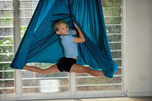 A young girl inverted in aerial yoga silk in monkey pose
