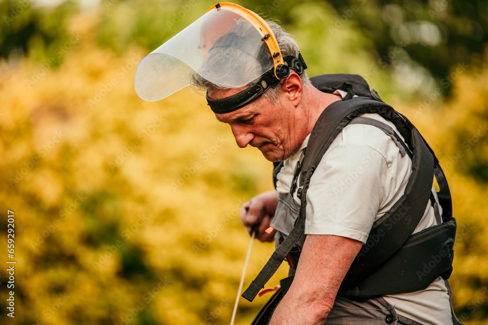 Fototapeta premium A seasoned gardener, this senior man gears up to trim the grass in his backyard