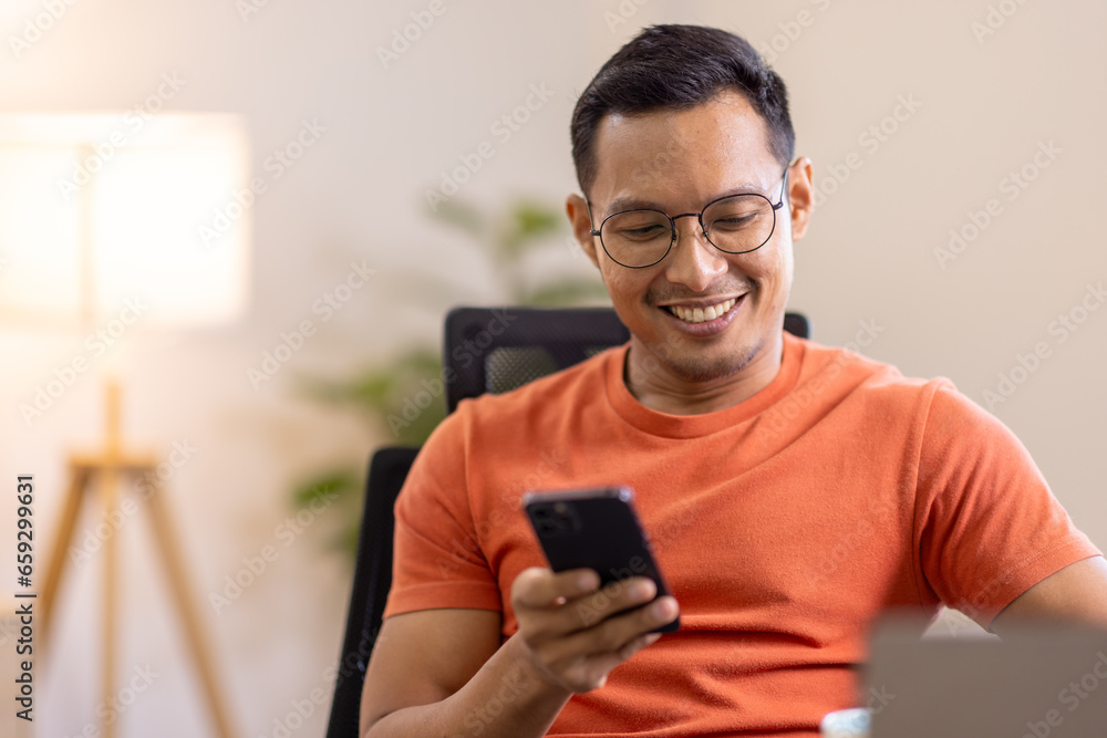 Picture of young asian man using a smartphone and smiling. working at home.accountant Documents data contract report for analysis TAX. Picture of young asian man using a smartphone and smiling. working at home.accountant Documents data contract report for analysis TAX.
