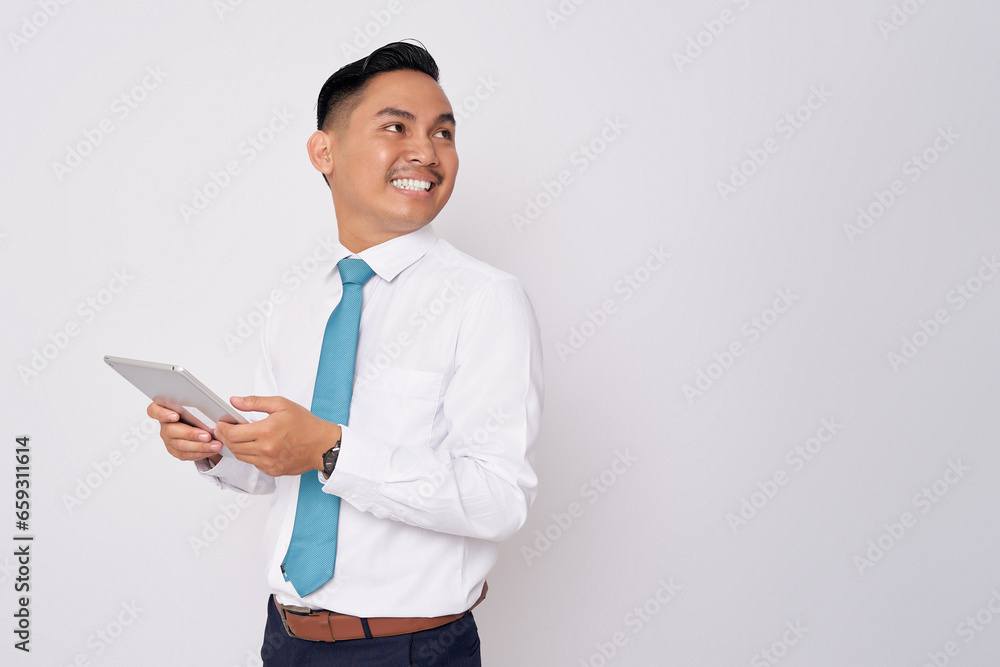 Portrait of smiling happy young Asian man in formal wear holding digital tablet and looking at side copy space for advertisement isolated on white background Portrait of smiling happy young Asian man in formal wear holding digital tablet and looking at side copy space for advertisement isolated on white background