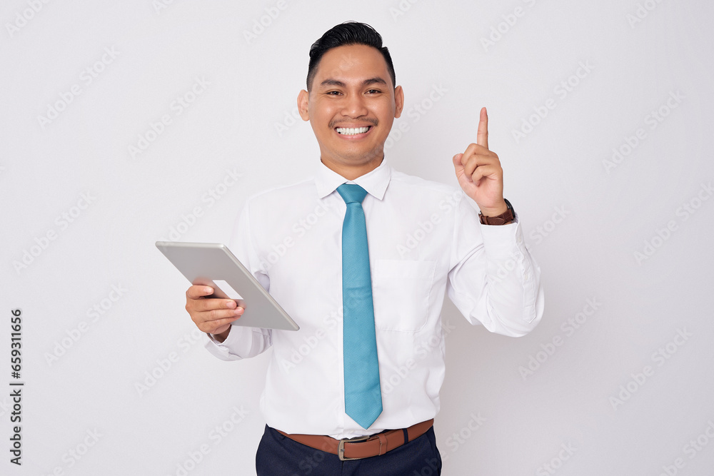 Portrait of excited young Asian man in formal wear pointing finger up getting idea after reading an article on tablet, solution on the problem in office isolated on white background Portrait of excited young Asian man in formal wear pointing finger up getting idea after reading an article on tablet, solution on the problem in office isolated on white background