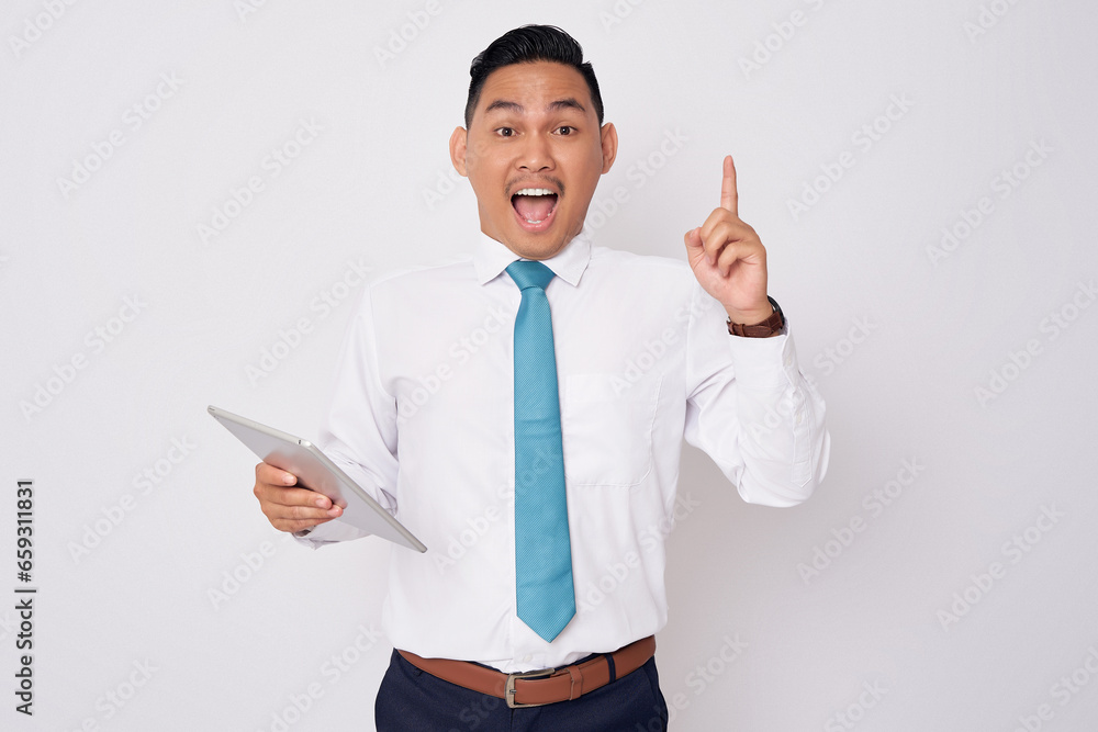 Portrait of excited young Asian man in formal wear pointing finger up getting idea after reading an article on tablet, solution on the problem in office isolated on white background