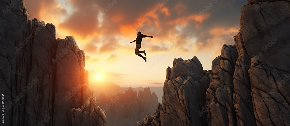 Businessman jumping over a cliff with a sunset in the background. - obrazy, fototapety, plakaty 