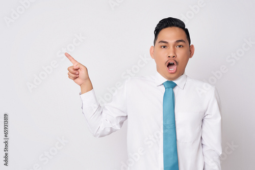 Portrait of surprised young Asian man in formal wear standing pointing fingers aside at copy space for advertisement and open mouth isolated on white background