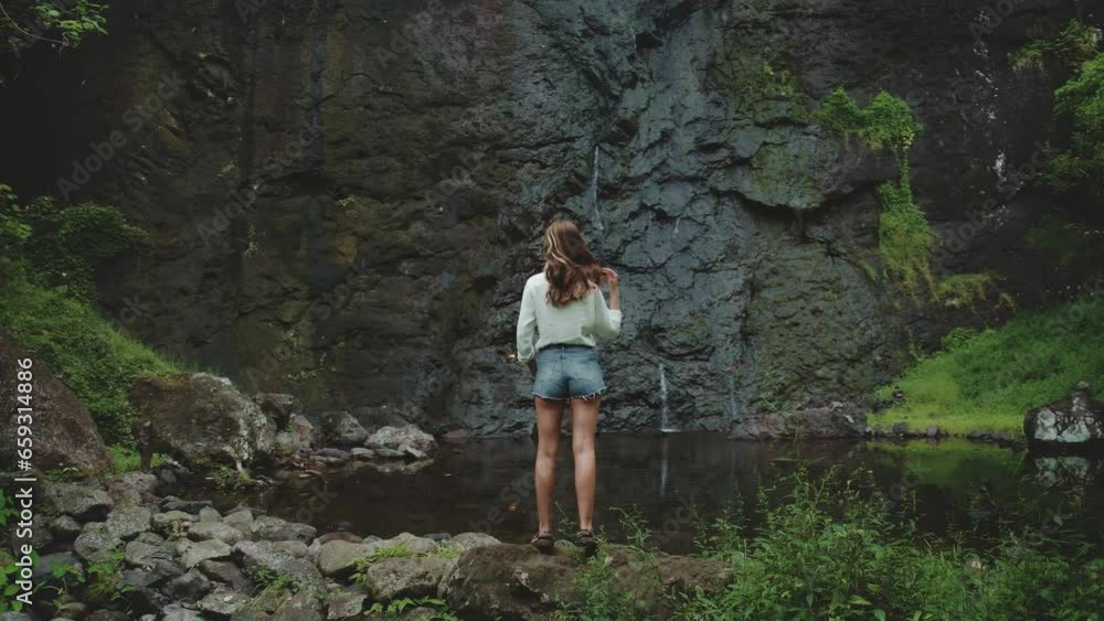 Tourist woman enjoy jungle waterfall landscape standing on rock stone. Girl relax outdoor lifestyle travel on summer holiday vacation. Picturesque scene panoramic shot. Dramatic dark toning, back view Tourist woman enjoy jungle waterfall landscape standing on rock stone. Girl relax outdoor lifestyle travel on summer holiday vacation. Picturesque scene panoramic shot. Dramatic dark toning, back view