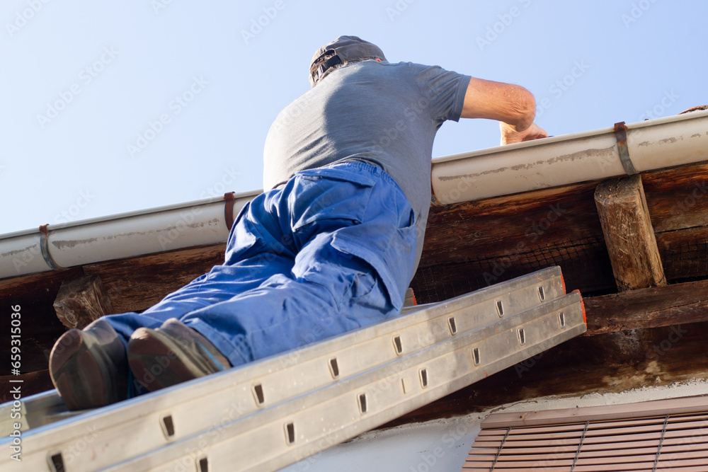 bricklayer construction worker on metalic staircase to repair old tile roof - obrazy, fototapety, plakaty 