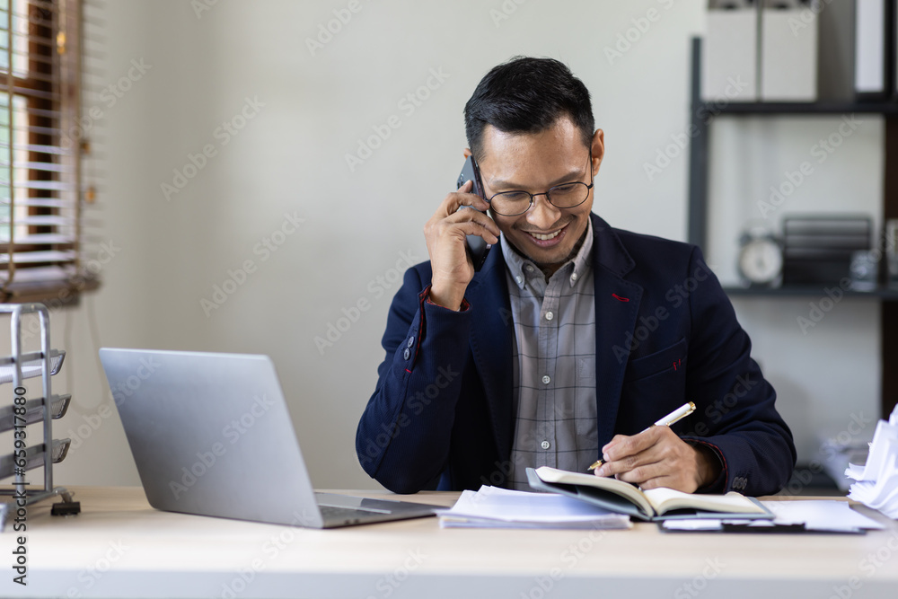 Obraz premium Inspiring productivity with a wealth of technology. Shot of a young business asian man talking on his phone and using a laptop during a late night at work.
