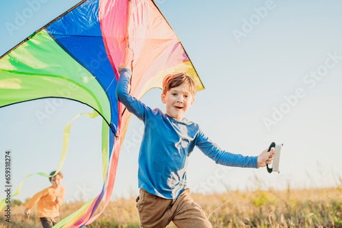 Smiling boy holding kite with brother running in field under sky photo