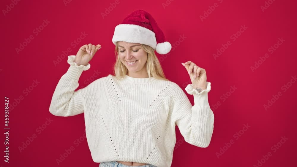 Young blonde woman wearing christmas hat dancing over isolated red background Young blonde woman wearing christmas hat dancing over isolated red background
