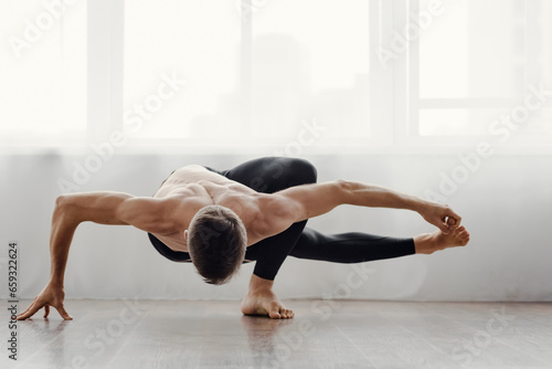 Athletic fit yoga man training in front of big light window, Robust sportsman assumes yoga position, demonstrating flexibility.