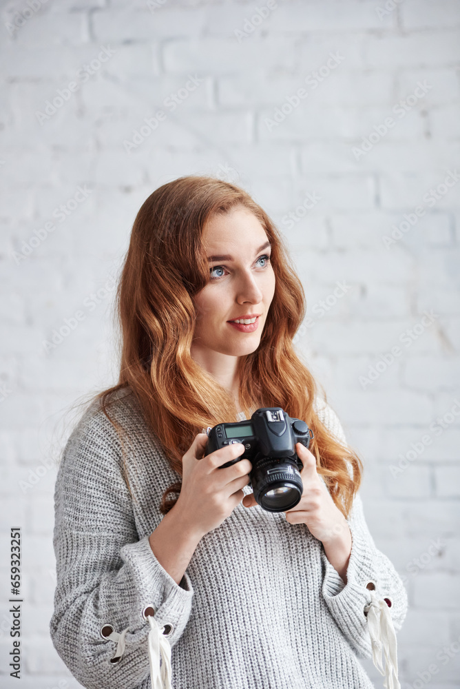 Portrait of beautiful smiling redhead girl posing with professional camera, Red-haired model beams, showcasing her skills with a camera.