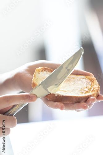 A piece of bread with butter in a woman's hand.