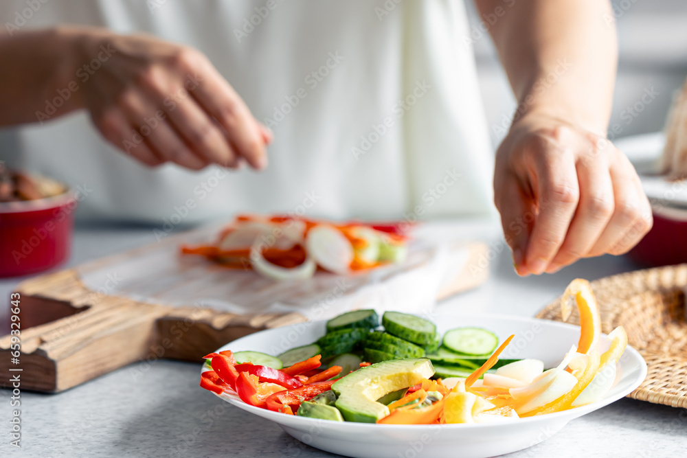 Woman preparing spring rolls in rice paper on kitchen table.