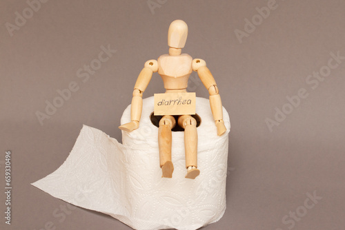 A wooden maniken sits on a roll of toilet paper labeled diarrhea, demanstrating bowel problems. photo