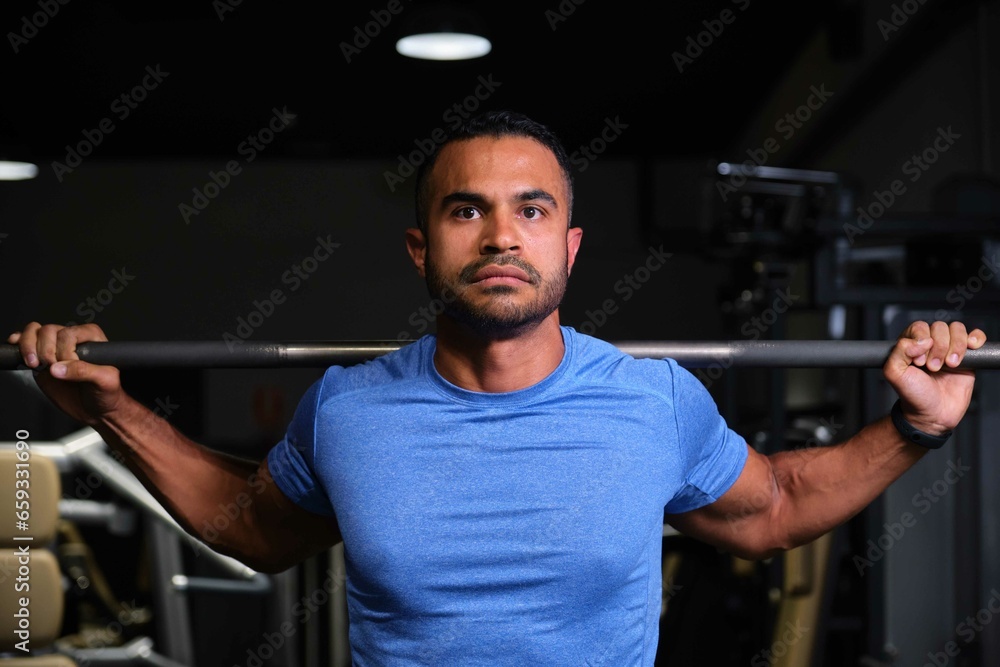 Fototapeta premium Portrait of a strong Hispanic man weightlifting at a gym.