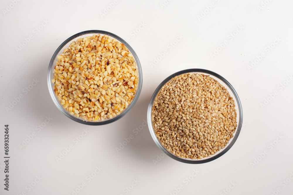 sesame seeds and chopped hazelnuts in a glass bowl on a white background shot from above sesame seeds and chopped hazelnuts in a glass bowl on a white background shot from above