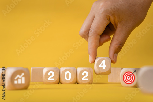 Business growth goals and success goals, hand holding wooden blocks with numbers, year 2024, graph icons, red targets. Business target or goal success and winner concept.