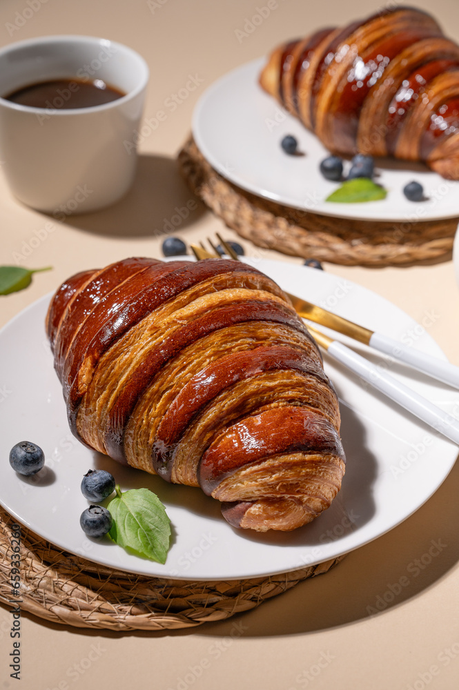 Freshly baked croissants with chocolate on a white plate and blueberries on a yellow background with cup of black coffee close up. Freshly baked croissants with chocolate on a white plate and blueberries on a yellow background with cup of black coffee close up.