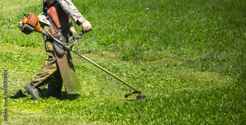 A man mows green grass with a petrol trimmer