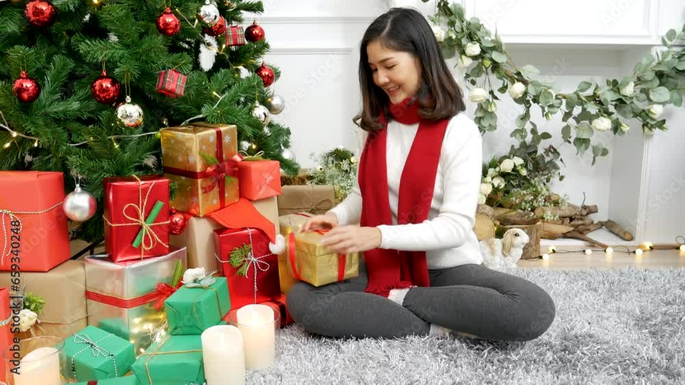Woman wrapping christmas gift box under xmas tree. Asian woman decor bauble ball christmas tree in xmas holiday winter seasonal celebration. Close up woman hands wrap present gift in cozy living room Woman wrapping christmas gift box under xmas tree. Asian woman decor bauble ball christmas tree in xmas holiday winter seasonal celebration. Close up woman hands wrap present gift in cozy living room