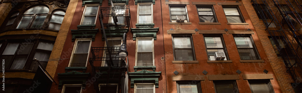 Obraz premium low angle view of vintage red brick house with fire escape stairs in new york city, banner