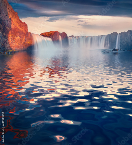 Godafoss waterfall reflected in the calm waters of Skjalfandafljot river. Majestic summer sunrise in Iceland, Europe. Beauty of nature concept background.