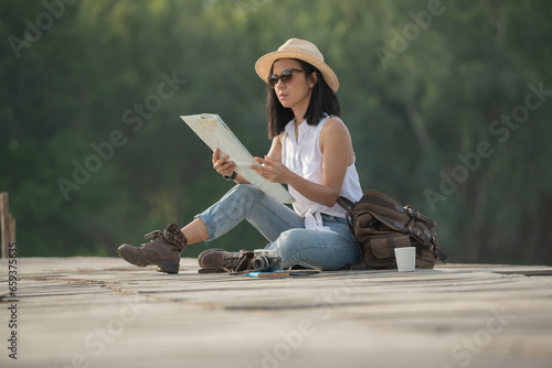 asian woman traveler with map backpack relaxing outdoor with sitting on quayside searching location on map during coffee break on background summer vacations and lifestyle hiking concept.