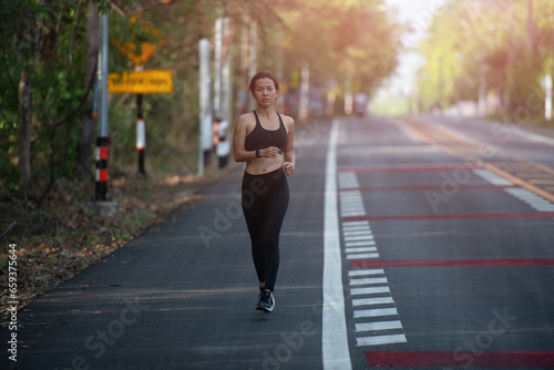 young fitness woman runner athlete running at road. athlete woman in running start pose on city street. sport tight clothes. bright sunset, horizontal. Healthy woman on morning road workout jogging. © nareekarn