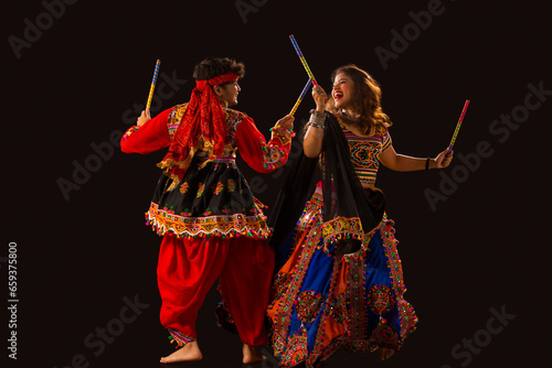 A  happy young couple performing Dandiya Raas on a black background, during Navratri celebrations photo