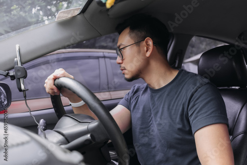 Asian Thai man with beard, wear eyeglasses parking a car, looking at car side mirror while driving training.