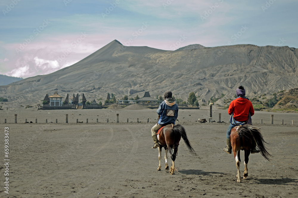 two adult man riding horses near a Hindu temple at Bromo Tengger National Park, East Java, Indonesia.