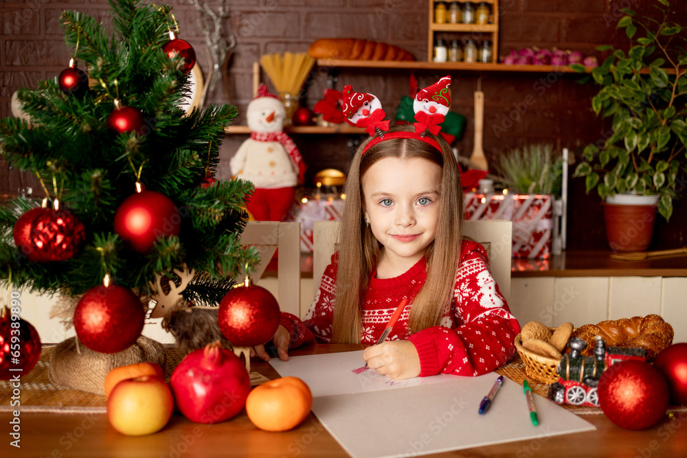 a child girl writes a letter to Santa Claus in a dark kitchen under a Christmas tree with red balls, the concept of new year and Christmas