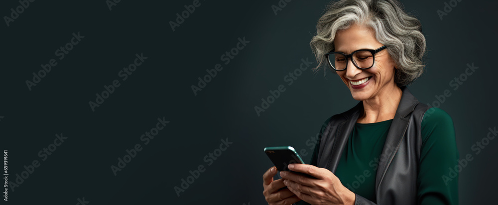 An elderly woman smiling and laughing with her phone against a colored background with copy space