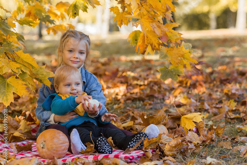 Portrait of a little boy 9 months old and a girl 4 years old outdoors. Happy children in the autumn park with pumpkins. Happy childhood and fatherhood.