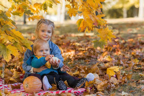 Portrait of a little boy 9 months old and a girl 4 years old outdoors. Happy children in the autumn park with pumpkins. Happy childhood and fatherhood.