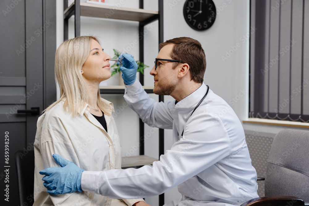 Obraz premium A young attractive otolaryngologist examining nose of a young patient during a medical examination in the ENT office