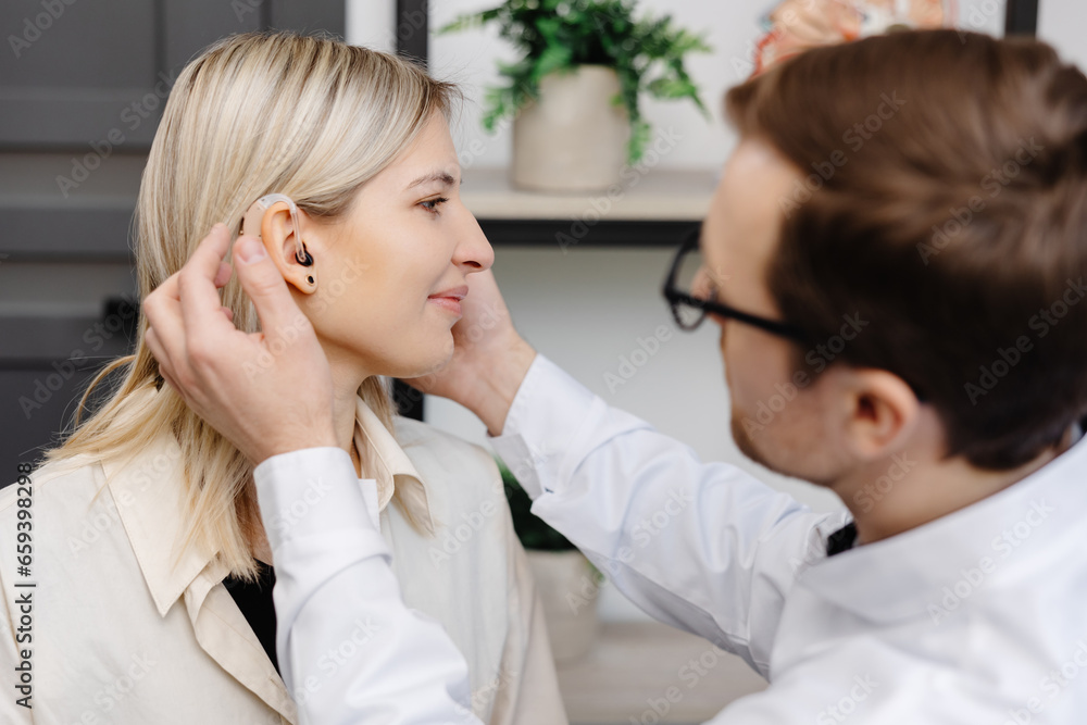 A young attractive otolaryngologist doctor gives a consultation to a female patient. A doctor explains how to wear a hearing aid to a woman
