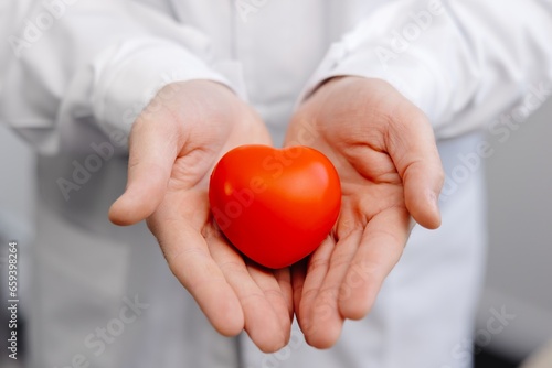 Doctor in white coat holding a red heart in hands close up. Medical health care and doctor staff service concept